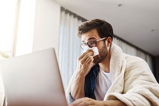 A person blowing their nose sitting at a computer